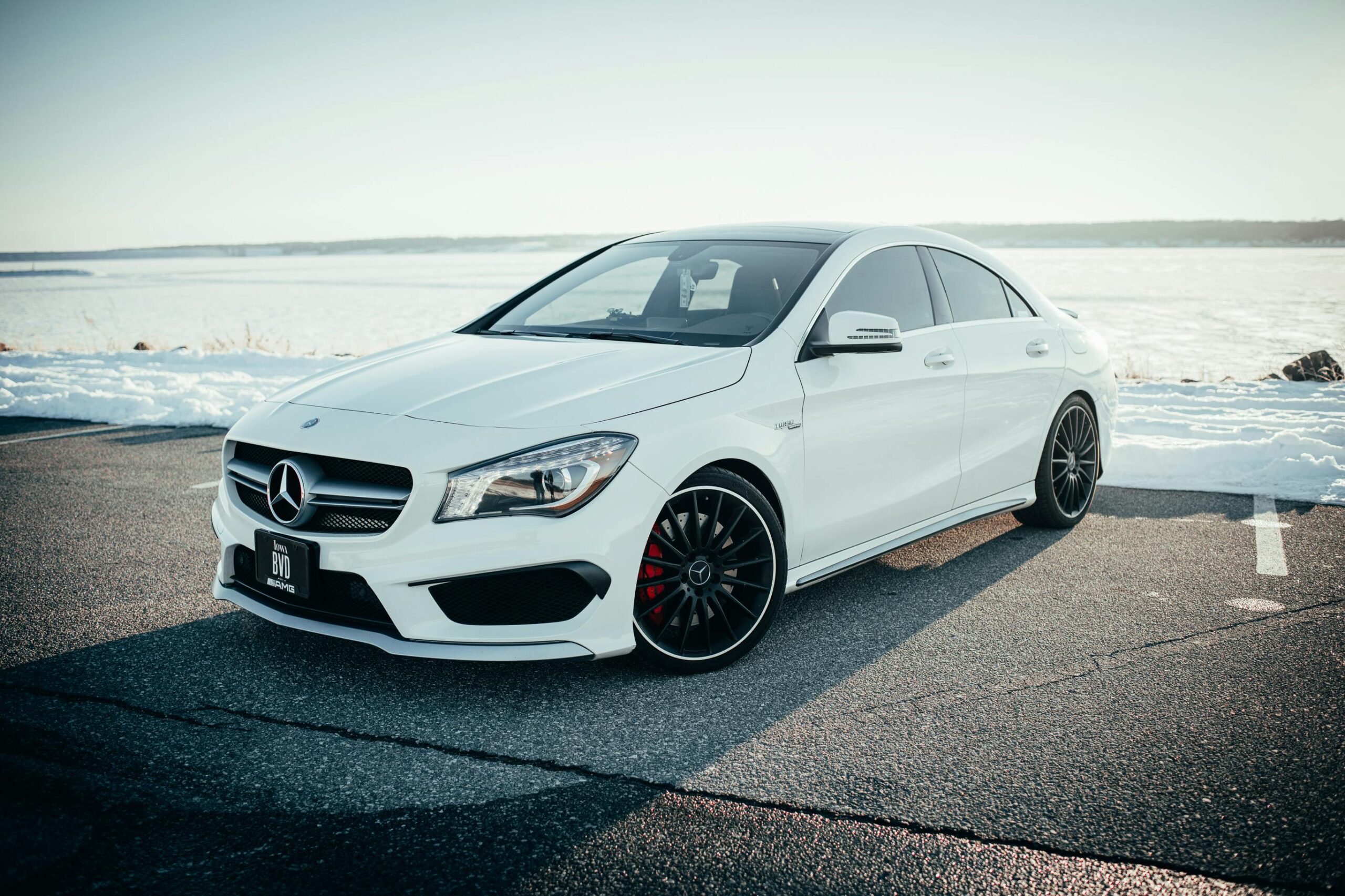 Sleek white Mercedes Benz sedan parked on a snowy road with a tranquil background.